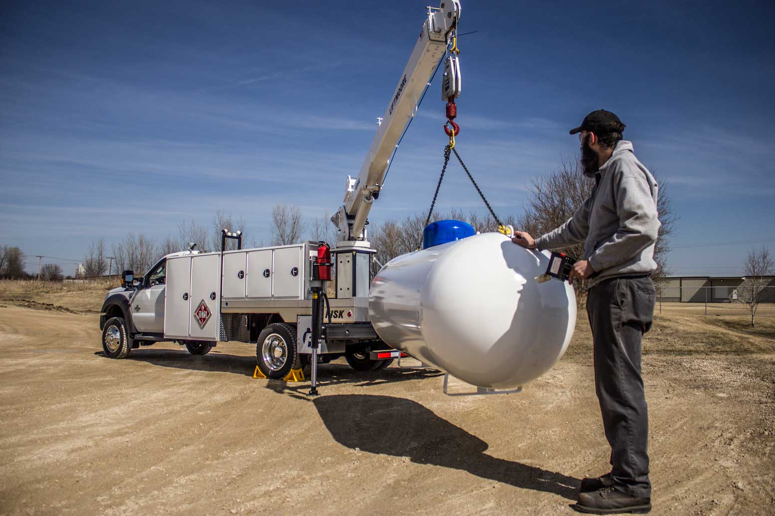 Serviceman lifting a propane tank with boom truck
