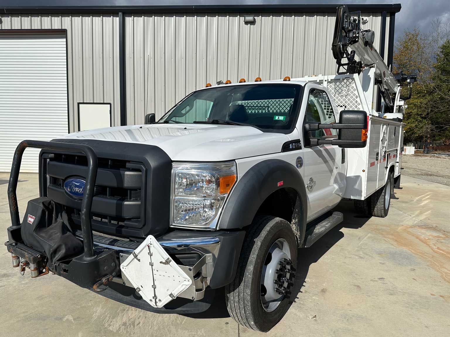 A white ford utility truck with a crane is parked in front of a building