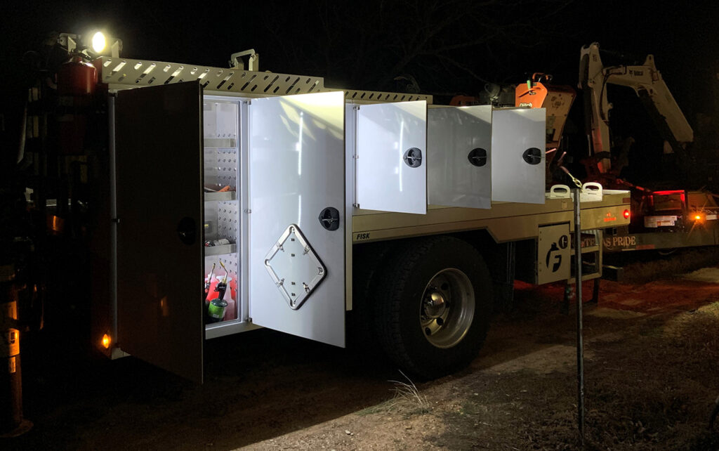 Image contains storage boxes on side of Fisk truck open and lights on inside the boxes.