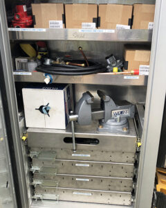 Image shows the inside of a storage box on a Fisk propane tank truck. The inside of the storage box has shelves and a vice mounted on the top of metal drawers.
