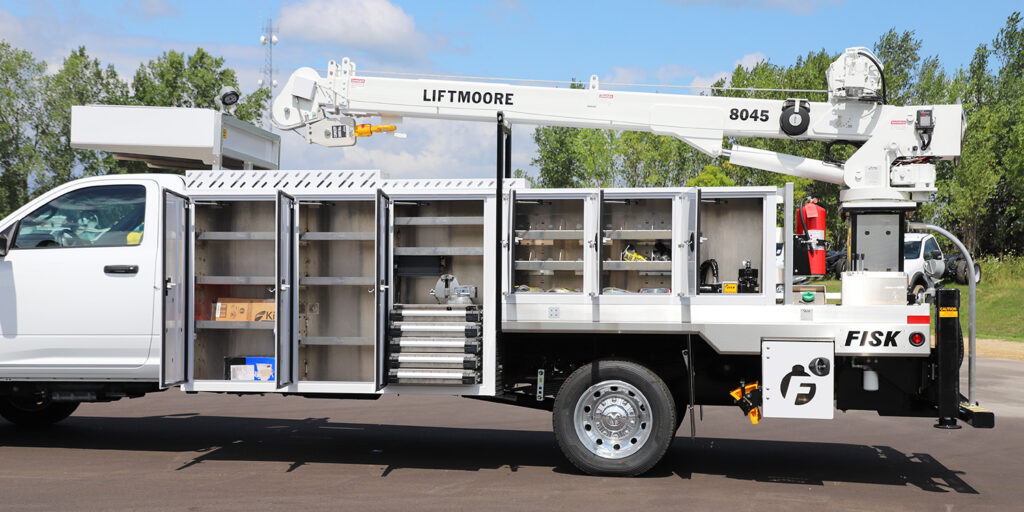 Image shows the driver side of a Fisk Tank Carrier TX-2 with all of the side storage boxes open.  It has a Liftmoore stick boom on it and a white cab and white overcab box.
